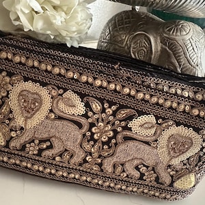 Peut inclure: Pochette noire avec broderies complexes représentant deux lions, des motifs floraux et des sequins dorés. Le sac est de forme rectangulaire et possède une bordure décorative. Le design est détaillé et orné, adapté aux occasions spéciales.