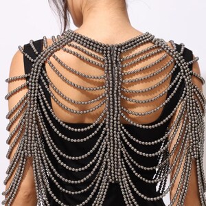 Model wearing a gunmetal beaded shoulder cape with cascading strands and sculptural drape over a black dress. This handmade capelet adds a bold, gothic touch to bridal, evening, or fashion looks.