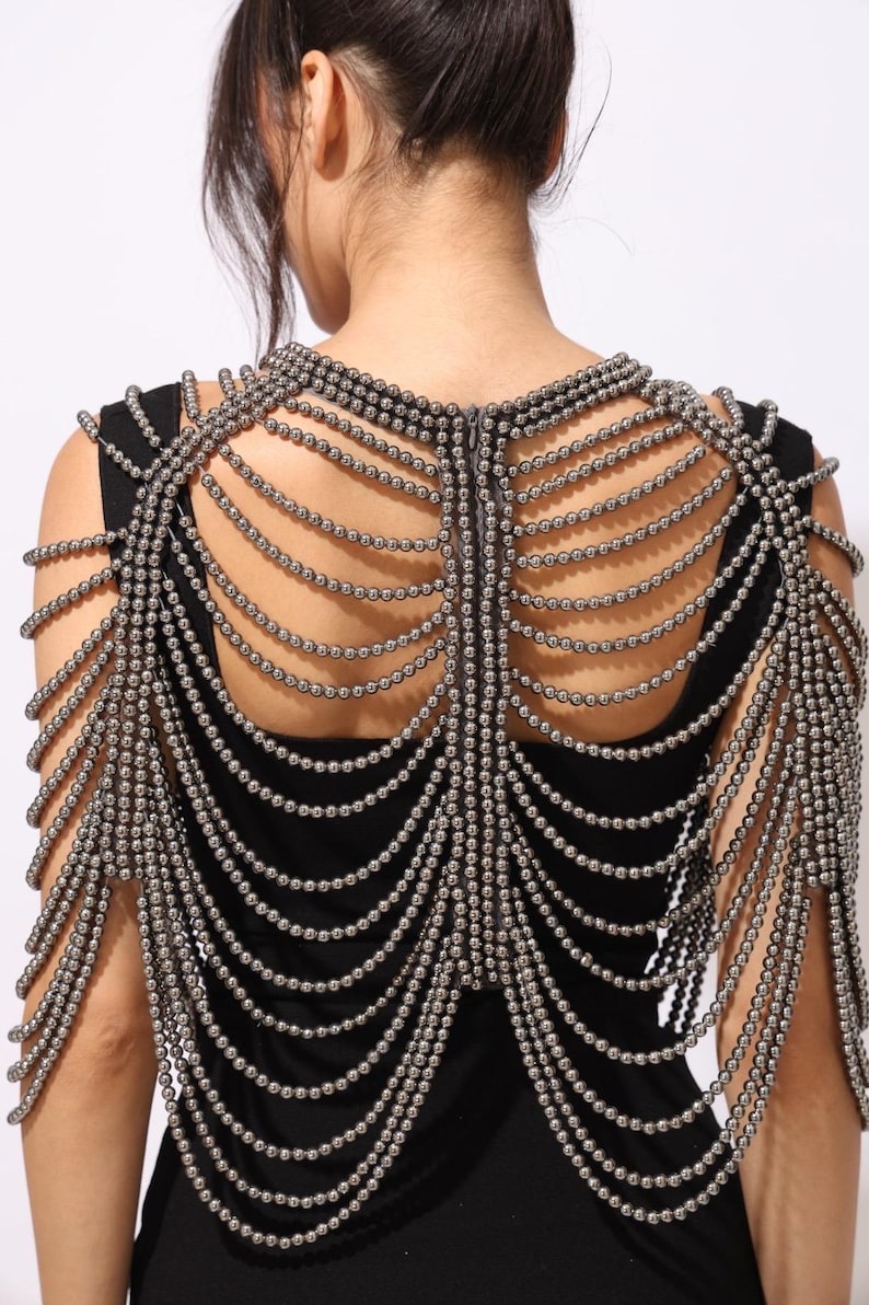 Model wearing a gunmetal beaded shoulder cape with cascading strands and sculptural drape over a black dress. This handmade capelet adds a bold, gothic touch to bridal, evening, or fashion looks.
