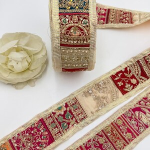 May include: A decorative fabric trim roll featuring a patchwork of vibrant red, pink, orange, and teal panels. The trim is heavily embellished with gold metallic thread, intricate floral embroidery, clear sequins, and small faux pearls throughout.