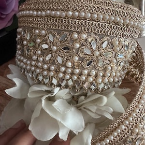 Close-up of gold lace trim with floral mirror work and pearl bead embellishments, ideal for sarees, bridal wear, and crafting.