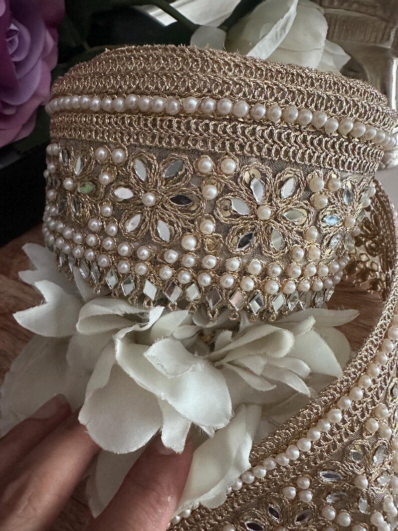 Close-up of gold lace trim with floral mirror work and pearl bead embellishments, ideal for sarees, bridal wear, and crafting.
