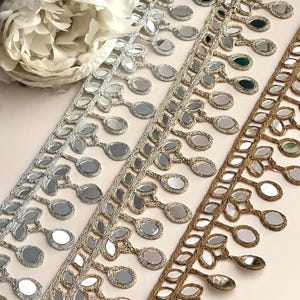 May include: Three rows of silver, gold, and bronze trim with mirrored embellishments. Each row features a fringe of oval-shaped mirrors with a beaded design.