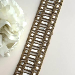 May include: Gold trim with rectangular mirror embellishments. The trim is made of a woven fabric with a metallic gold thread. The trim is approximately 1 inch wide.