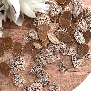 Könnte beinhalten: Eine Sammlung von goldenen und weißen Stoffverzierungen in Tropfenform. Die Verzierungen sind auf einer Holzoberfläche verstreut.