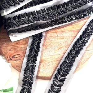 May include: Black beaded trim with a leaf design on a sheer mesh fabric. The trim is perfect for adding a touch of elegance to any project.
