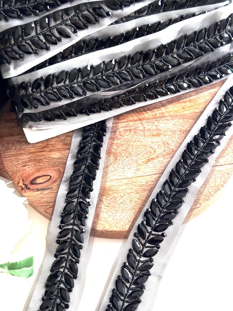 May include: Black beaded trim with a leaf design on a sheer mesh fabric. The trim is perfect for adding a touch of elegance to any project.
