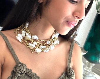 May include: A multi-strand necklace featuring large, irregular white pearls and gold-toned metal chains. The necklace is layered and sits close to the neck. The image shows a close-up of the necklace.