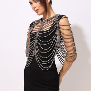 Model wearing a gunmetal beaded shoulder cape with cascading strands and sculptural drape over a black dress. This handmade capelet adds a bold, gothic touch to bridal, evening, or fashion looks.