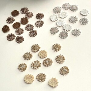 May include: A collection of small, sunflower-shaped fabric embellishments in various colors. The embellishments include shades of brown, silver, and gold. These decorative elements are likely used for crafts, sewing, or adding detail to clothing and accessories.