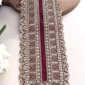 May include: Burgundy fabric trim with gold embroidery and sequins. The trim has a scalloped edge and a geometric design.
