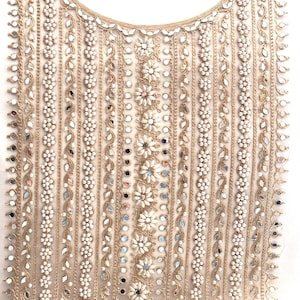 Può includere: Un colletto in tessuto beige con ricamo intricato che presenta filo dorato, piccoli specchi e perline bianche. Il design include motivi floreali e motivi geometrici.