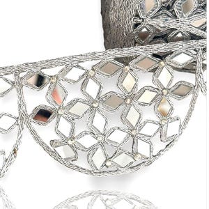 May include: Close-up of silver decorative trim with mirrored details. The trim has a repeating pattern of diamond-shaped mirrors set in a floral design, outlined with silver thread. It is likely used for embellishing clothing or crafts.