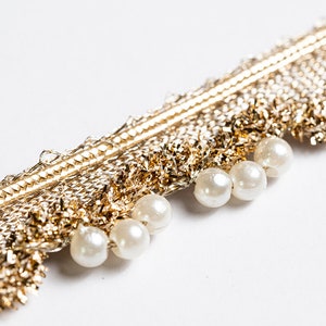 May include: Gold trim with a fringe of gold and white beads. The trim is perfect for adding a touch of elegance to any project.