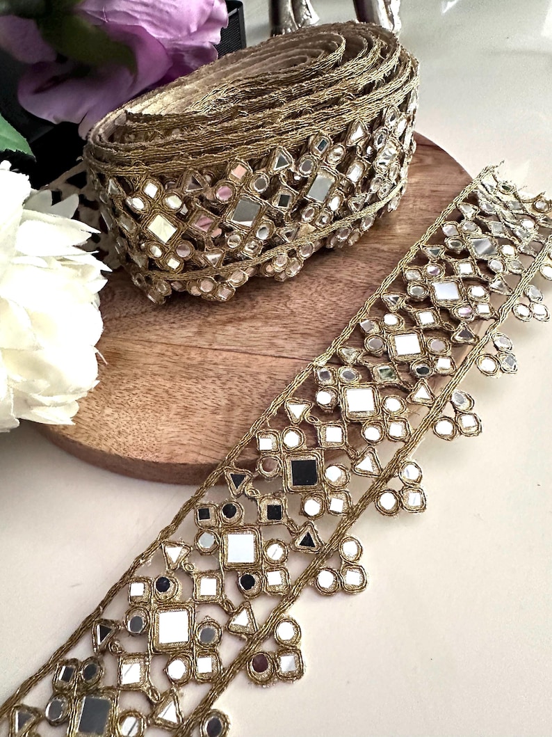 Close-up of gold mirror embroidered lace trim for bridal costume belts, featuring geometric mirror patterns and metallic threadwork.