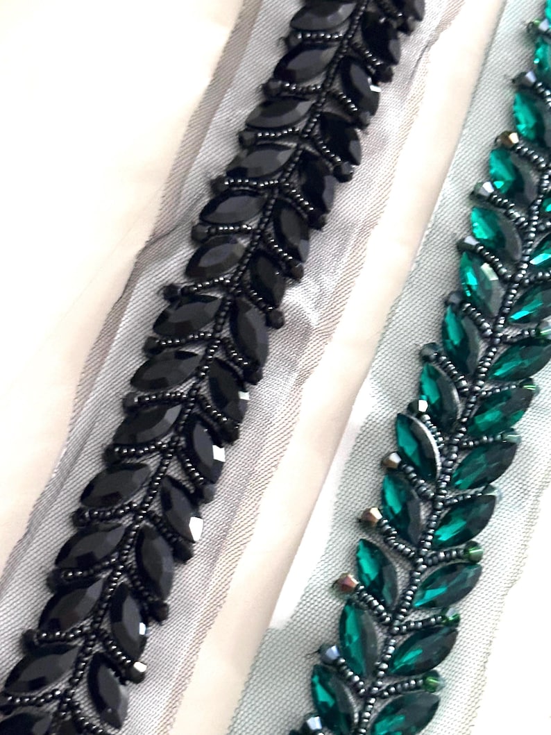 May include: Two beaded trims, one black and one green, with a leaf design. The trim is on a sheer fabric background.