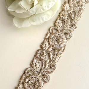 May include: Gold embroidered trim with a floral design. The trim features intricate details and a delicate, openwork pattern.