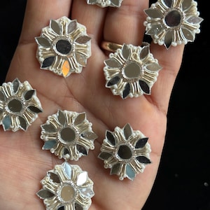 Puede incluir: Ocho adornos de tela en forma de flor de color blanco con un centro de espejo y ribete dorado. Cada flor tiene una perla nacarada en el centro de cada pétalo.
