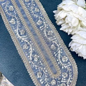 May include: A delicate, beaded trim with a gold and silver design. The trim features a repeating pattern of small flowers and leaves, with a scalloped edge.