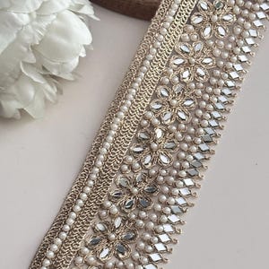 Elegant floral pearl lace trim with diamond mirror accents, shown at an angle with flower props, used in fashion or décor.