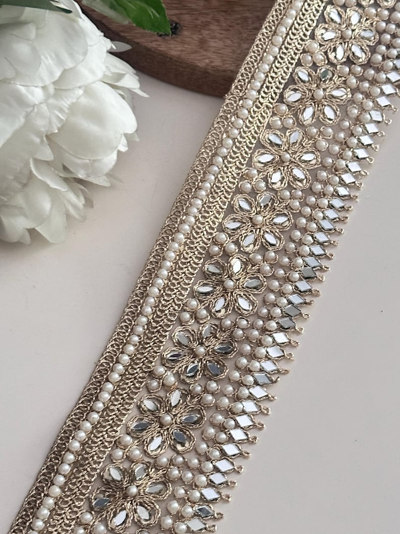 Elegant floral pearl lace trim with diamond mirror accents, shown at an angle with flower props, used in fashion or décor.