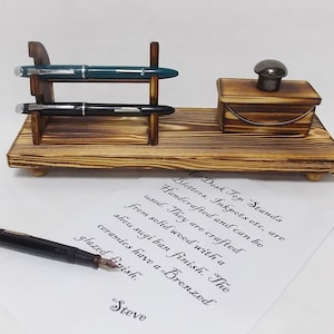 May include: Wooden desk top stand with two pen holders and an inkwell. The stand is made of solid wood with a shou sugi ban finish. The ceramics have a bronzed glazed finish. "All Desk Top Stands, Blotters, Inkpots etc, are Handcrafted and can be used. They are crafted from solid wood with a shou sugi ban finish. The ceramics have a Bronzed glazed finish. Steve"