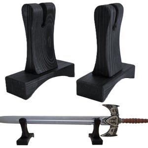 May include: Two black wooden sword stands and a sword. The stands are made of dark wood with a textured grain. The sword has a silver blade and an ornate handle with brown and silver details.