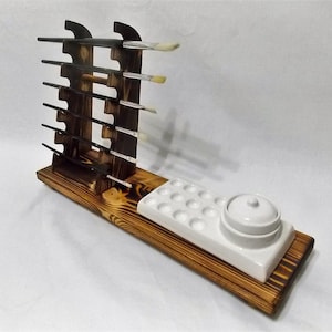 May include: Wooden paintbrush holder with a dark wood finish and a white ceramic paint palette with a lid. The holder has slots for multiple paintbrushes and the palette has 18 wells.