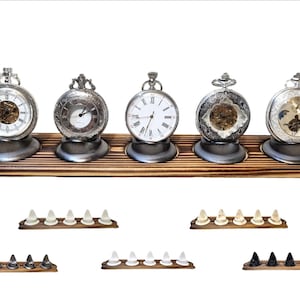 Pode incluir: Cinco relógios de bolso antigos com caixas prateadas e mostradores brancos, expostos numa prateleira de madeira. Abaixo, vários conjuntos de pequenos objetos decorativos em várias cores, também em bases de madeira.