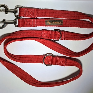 May include: Red double dog lead with two silver clips and two silver D-rings. The lead has the word "CORREA" printed on it.