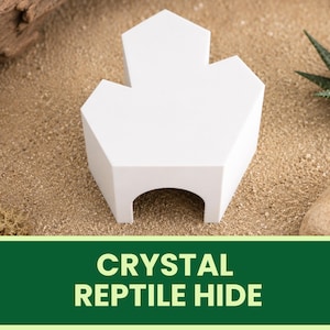 May include: A white, geometric reptile hide with a clover-like top and an arched opening. The hide is set on a sandy surface with a small succulent plant and a rock in the background. The text "CRYSTAL REPTILE HIDE" is displayed on a green banner.