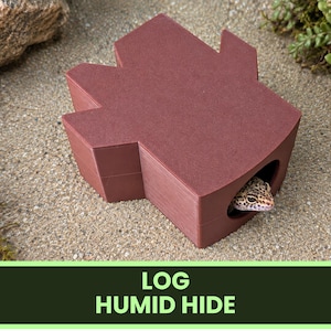 May include: A brown, matte-finished, log-shaped reptile hide with a multi-pointed top and a rounded entrance hole. A small, spotted leopard gecko is visible peering out from the interior of the structure. The text LOG HUMID HIDE is displayed.