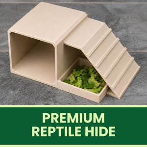 Op de afbeelding: Een beige reptielenschuilplaats met een holle kubusvormige schuilplaats verbonden aan een helling met daaronder een kleine vierkante voerbak. De bak bevat groene bladgroenten. De tekst PREMIUM REPTILE HIDE staat in het wit op een groene banner.