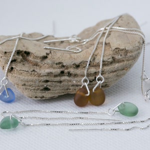May include: Four pairs of silver chain earrings with different coloured glass teardrop charms. The charms are blue, green, amber, and clear.