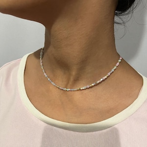 Peut inclure: Un délicat collier de perles composé d'un mélange de perles aux couleurs pastel, notamment roses, bleues et aux reflets irisés. Le collier est monté sur un cordon fin et souple et est conçu pour se porter près du cou. Les perles sont petites et espacées uniformément.