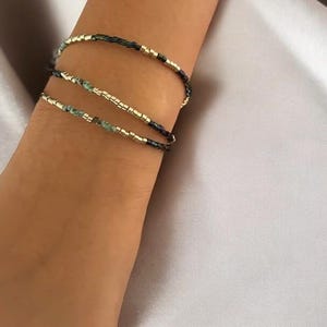 Peut inclure: Trois bracelets superposés avec des perles dorées, noires et vertes.
