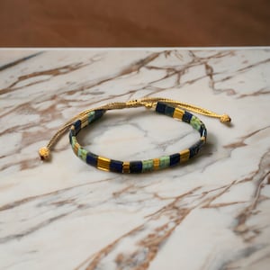 Peut inclure: Un bracelet en perles bleues, vertes et dorées avec un cordon doré et un fermoir réglable.