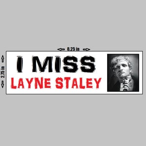 May include: A rectangular bumper sticker that is 8.25 inches wide and 2.75 inches tall. The sticker has the words "I MISS LAYNE STALEY" in black and red text. A black and white photo of a man holding a microphone is on the right side.
