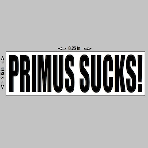 Może przedstawiać: Prostokątna naklejka z napisem "PRIMUS SUCKS!" pogrubionymi, czarnymi literami. Naklejka ma 21 cm szerokości i 7 cm wysokości, z białym obramowaniem i szarym tłem.