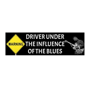 May include: Black bumper sticker with the text "DRIVER UNDER THE INFLUENCE OF THE BLUES." A yellow warning sign is on the left, and a black and white image of a musician playing a guitar is on the right.