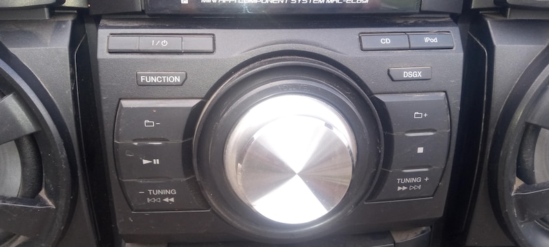 Peut inclure: Une mini-cha&icirc;ne st&eacute;r&eacute;o noire avec un gros bouton central argent&eacute; et divers boutons de fonction. Le syst&egrave;me comprend des boutons pour CD, iPod et commandes de r&eacute;glage. L'&eacute;cran affiche du texte en haut.