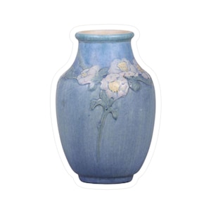 May include: A blue ceramic vase with a textured surface. The vase features a floral relief design with white and yellow flowers and green leaves. The vase has a light blue rim.