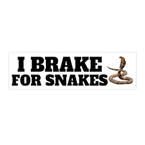 以下が含まれることがあります： 太字の黒い文字で「I BRAKE FOR SNAKES」と書かれた白い長方形のステッカー。茶色のコブラヘビがステッカーの右側にあります。
