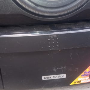 Peut inclure: Syst&egrave;me st&eacute;r&eacute;o noir avec un haut-parleur et une station d'accueil pour iPod. Le syst&egrave;me comporte un bouton "PUSH" et un autocollant indiquant "Dock for iPod" et "100w". Le syst&egrave;me a un cordon d'alimentation.