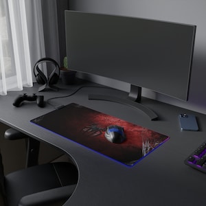 May include: A black computer desk with a black computer monitor, a black gaming headset, a black and red gaming mouse pad with a spider web design, a black gaming mouse, a black controller, and a black smartphone.