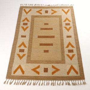 Peut inclure: Tapis rectangulaire beige avec un motif géométrique. Le tapis présente un champ central beige avec des lignes et des carrés horizontaux marron. La bordure est beige avec des formes géométriques marron et des franges aux extrémités courtes.