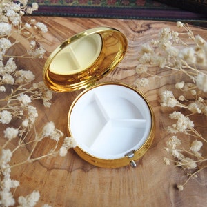 K&ouml;nnte beinhalten: Goldene Pillendose mit drei F&auml;chern. Die Dose ist ge&ouml;ffnet und die F&auml;cher sind leer.