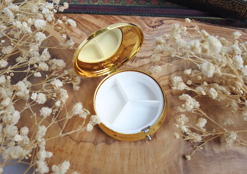 K&ouml;nnte beinhalten: Goldene Pillendose mit drei F&auml;chern. Die Dose ist ge&ouml;ffnet und die F&auml;cher sind leer.