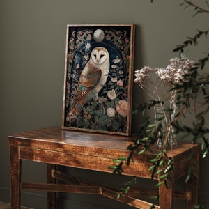 May include: Framed art print featuring a detailed illustration of an owl with a white face and brown and tan feathers, surrounded by flowers and foliage. The artwork is set against a dark blue background and framed in a wooden frame. The print is displayed on a wooden table.
