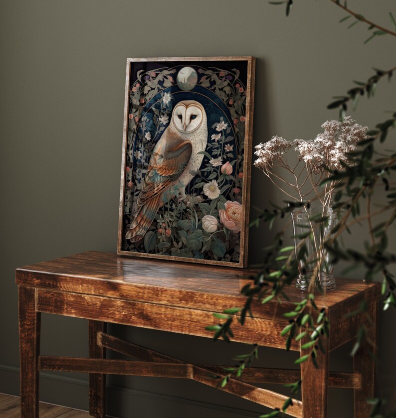 May include: Framed art print featuring a detailed illustration of an owl with a white face and brown and tan feathers, surrounded by flowers and foliage. The artwork is set against a dark blue background and framed in a wooden frame. The print is displayed on a wooden table.